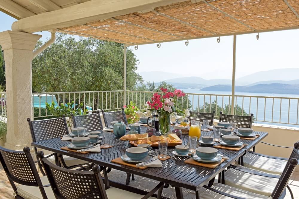 Covered outdoor dining terrace at Villa Eremia with long table set for al fresco meals overlooking the Ionian Sea, Corfu