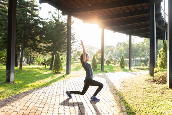 Woman performing a deep lunge stretch outdoors in a sunlit garden, representing the wellness and fitness experience at Eremia, Corfu