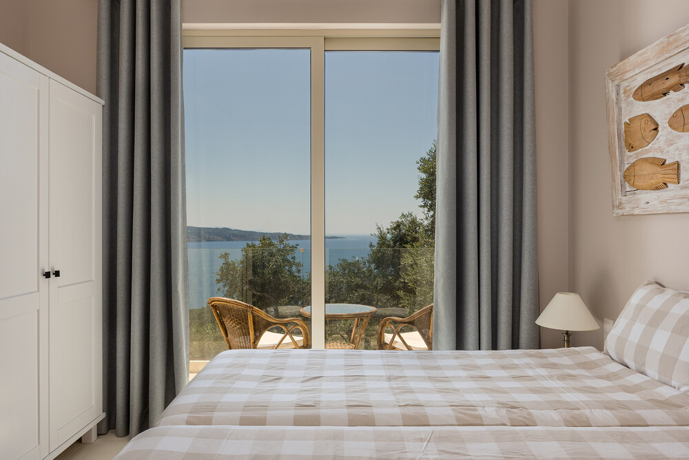 Bedroom at Elyonas Cottage with checkered linens and full-height window opening to sea views