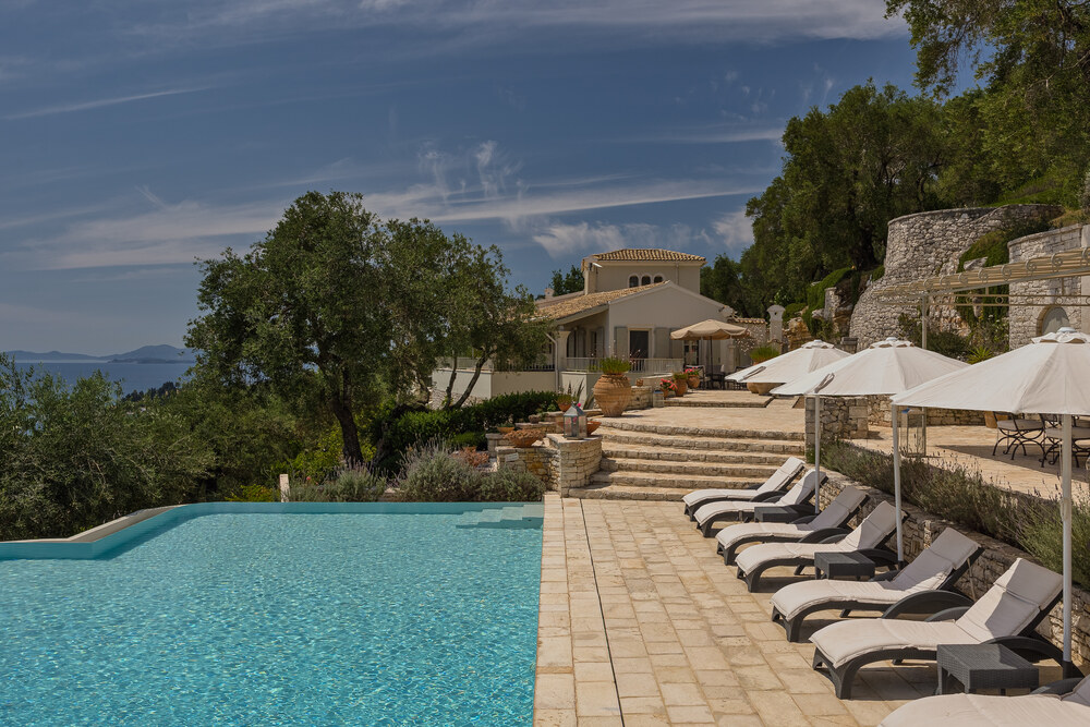 Infinity pool and sun loungers at Villa Eremia, Corfu, offering a peaceful setting for wellness and recovery with sea views beyond