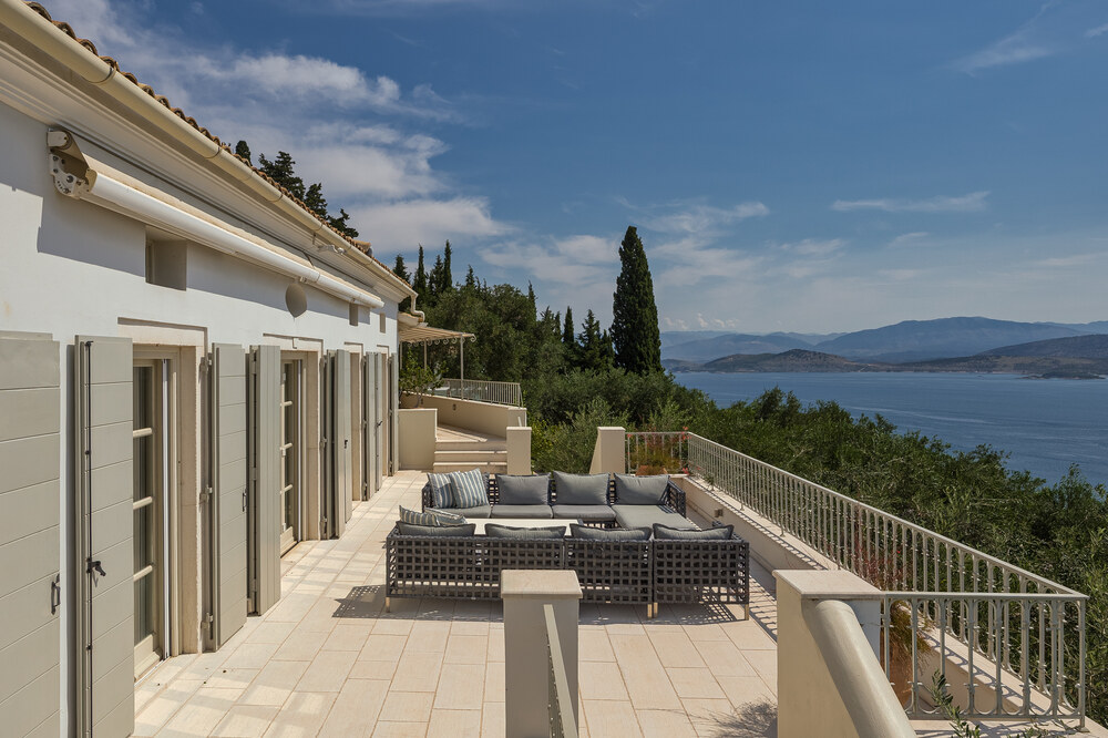 Open terrace at Villa Eremia, Corfu, with outdoor lounge seating and panoramic sea views stretching to distant mountains